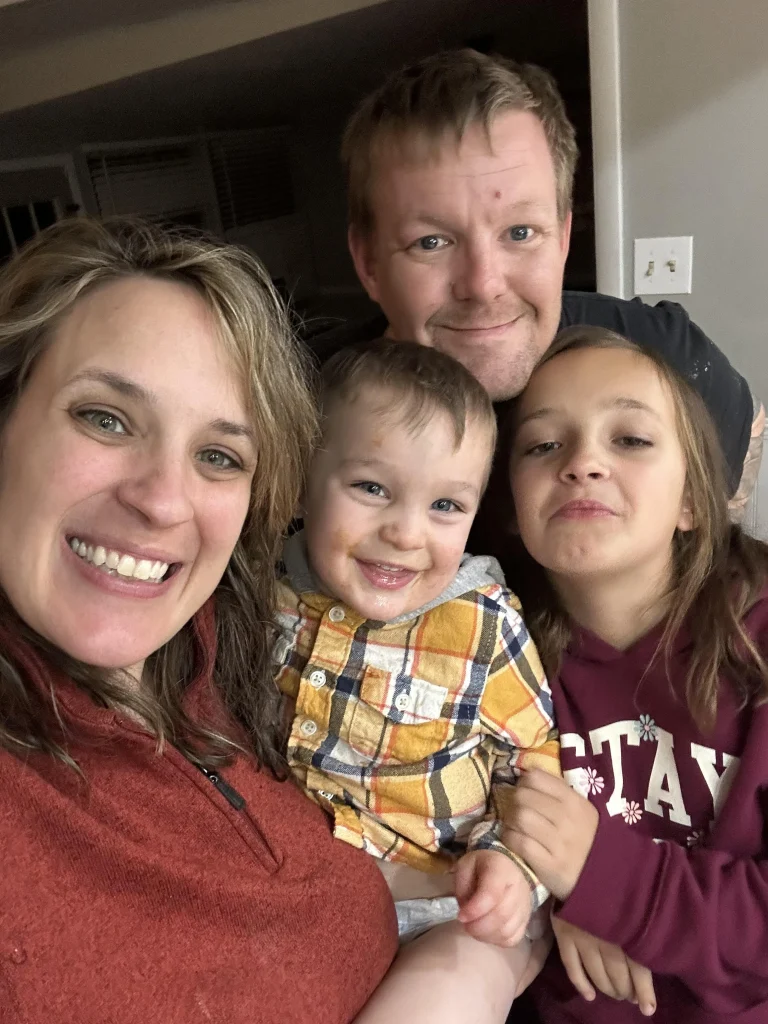 Stephanie smiling with her partner and two young children in a cozy indoor family photo.